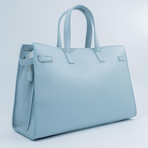 May include: A light blue leather handbag with two top handles and a structured design. The bag features a zipper closure and a textured surface. The handbag has a rectangular shape and is suitable for everyday use.