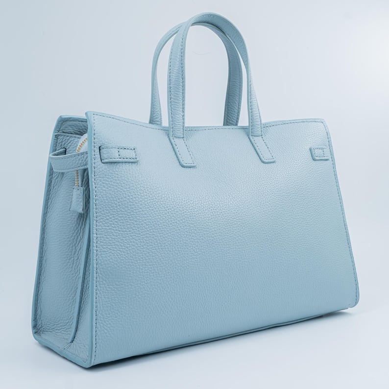 May include: A light blue leather handbag with two top handles and a structured design. The bag features a zipper closure and a textured surface. The handbag has a rectangular shape and is suitable for everyday use.