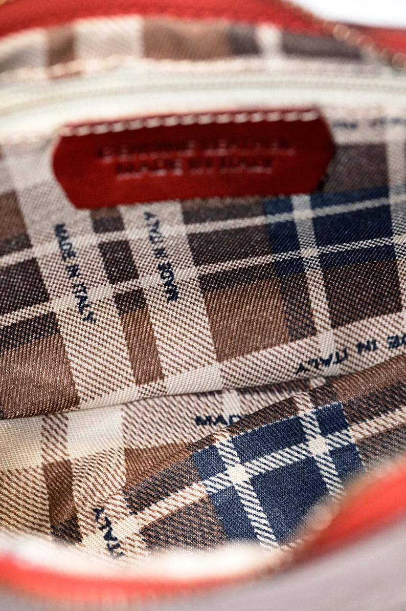 May include: The inside of a red leather bag with a plaid lining. The lining has the text "Made in Italy" printed on it.
