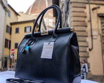 Op de afbeelding: Zwarte leren handtas met een gouden slot en een label met de tekst "Genuine Leather -  'eccellenza in pelle' - Made in Italy".