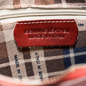 May include: Close-up of a red leather purse lining with a red leather tag that reads "GENUINE LEATHER MADE IN ITALY".