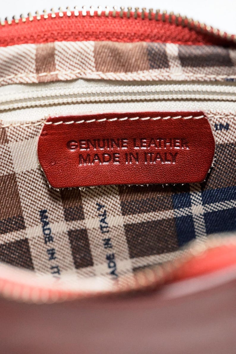 May include: Close-up of a red leather purse lining with a red leather tag that reads "GENUINE LEATHER MADE IN ITALY".