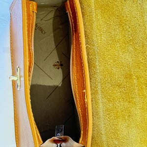 May include: Inside view of a brown leather handbag with a zipper closure. The interior is lined with a beige fabric and has a label that reads "Made in Italy".