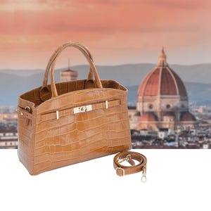 May include: A tan leather handbag with a crocodile texture, featuring a top handle and a detachable shoulder strap. The bag has a rectangular shape with a flap closure and gold-colored hardware. The background shows a blurred cityscape.
