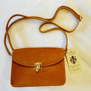 May include: A small brown leather crossbody bag with a gold clasp and a tag that reads "Florentine Leather, Genuine Leather Made in Italy".