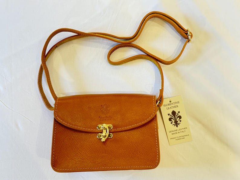 May include: A small brown leather crossbody bag with a gold clasp and a tag that reads "Florentine Leather, Genuine Leather Made in Italy".