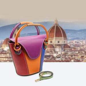 May include: A multi-coloured leather handbag with a bucket shape. The bag features red, orange, purple, and blue panels, with a matching green shoulder strap. The handles are orange with a tan grip.