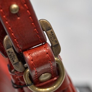 May include: Close-up of a red leather strap with a gold metal buckle. The buckle has the words "Made in Italy" engraved on it.