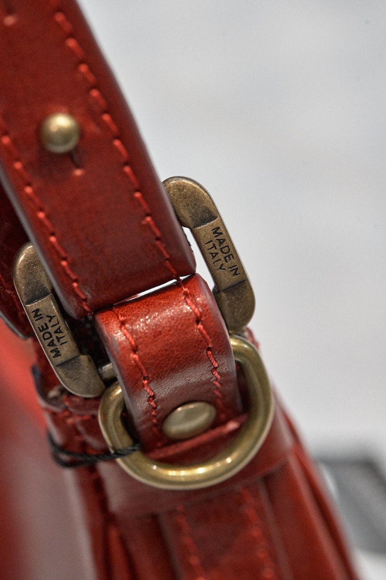 May include: Close-up of a red leather strap with a gold metal buckle. The buckle has the words "Made in Italy" engraved on it.