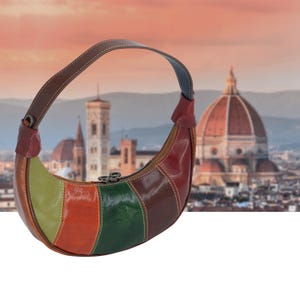 Peut inclure: Un sac à main en cuir en forme de croissant avec un design à panneaux multicolores dans des tons vert lime, orange, vert foncé et marron. Le sac comprend une bandoulière marron unique, une fermeture éclair et des coutures blanches.