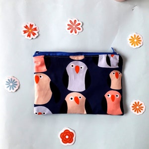 May include: A blue zippered pouch with a dark blue background and a repeating pattern of pink and gray birds with orange beaks.