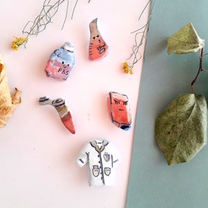 May include: A set of five hand-painted ceramic figurines. The figurines include a lab coat, a beaker, a test tube, a bottle labeled "PBS", and a small box with a face.