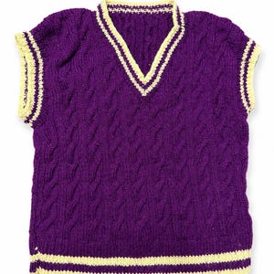 May include: A sleeveless V-neck sweater vest in a deep purple color featuring a cable knit pattern throughout. The neckline, armholes, and bottom hem are finished with a contrasting cream-colored ribbed trim with thin purple stripes.