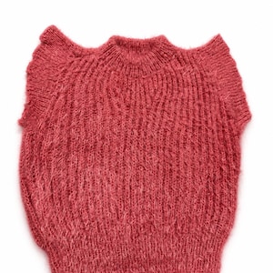 May include: A sleeveless knit sweater in a dusty rose color featuring a fuzzy, textured yarn composition. The garment has a ribbed crew neckline, ribbed armholes with a slight ruffle detail, and a ribbed hemline, all crafted in a vertical knit pattern.