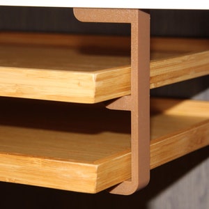 Puede incluir: Estantería de bambú de dos niveles con estructura de soporte marrón. Los estantes son de bambú de color claro y están soportados por un soporte marrón en forma de L. Los estantes están diseñados para montarse en una pared o dentro de un armario.