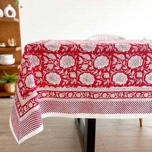May include: Red and white floral tablecloth with a white border and red stripes. The tablecloth is on a wooden table.
