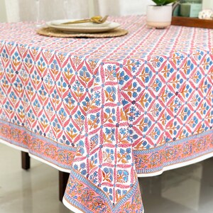 May include: A white tablecloth with a pink, blue, and orange floral pattern. The tablecloth has a border with a repeating pattern of leaves and flowers.