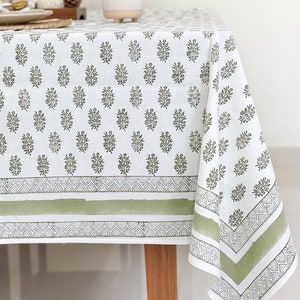 May include: A white tablecloth with a green floral pattern and a green border. The tablecloth is on a wooden table.