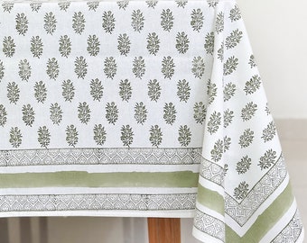 May include: A white tablecloth with a green floral pattern and a green border. The tablecloth is on a wooden table.