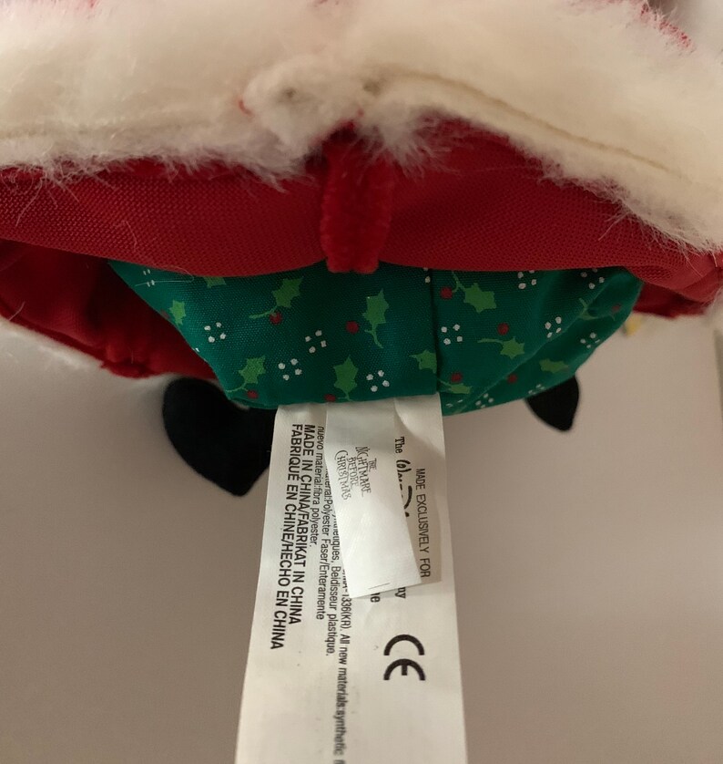 May include: A plush Santa Claus doll with a red coat, white trim, and a green patterned skirt. The tag reads "MADE IN CHINA" and "The (0) Nightmare Christmas". The doll has black boots and a white fluffy beard.