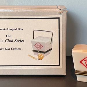 May include: A porcelain hinged box from The Men's Club Series, featuring a miniature take-out Chinese food container design. The box is white with a red "Take Out" logo and gold-colored accents. The box is next to its original packaging.