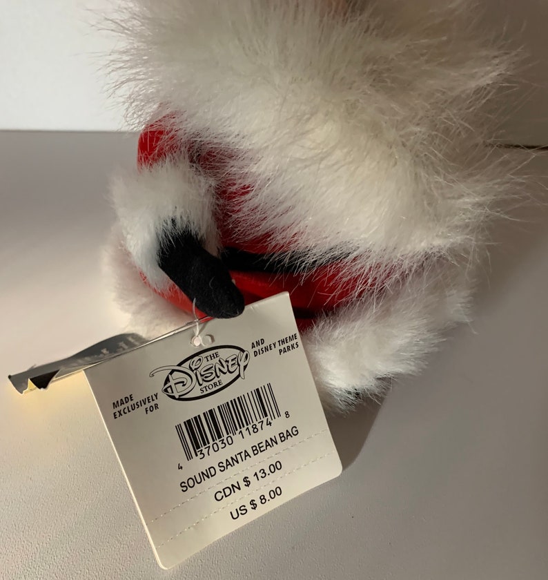 May include: A Disney Store Sound Santa Bean Bag. The plush toy is red with white faux fur trim and black accents. The attached tag reads "SOUND SANTA BEAN BAG".