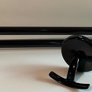 May include: Black metal double towel bar with a single hook on the end. The towel bar is mounted to a wall.