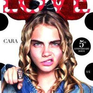 May include: A magazine cover featuring a woman with blonde curly hair wearing a red and white polka dot headband. The magazine cover says "LOVE" in large red letters and "CARA" in black letters. The magazine is celebrating its 5th anniversary.