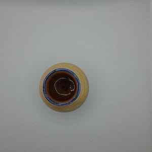 K&ouml;nnte beinhalten: Ein kleiner, runder, gelber Keramiktopf mit blauem Rand. Der Topf hat einen braunen Innenraum und ist leer.