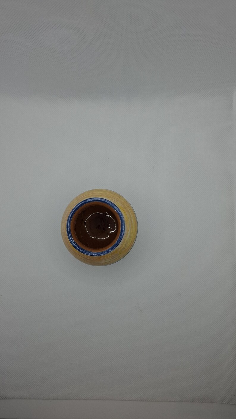 K&ouml;nnte beinhalten: Ein kleiner, runder, gelber Keramiktopf mit blauem Rand. Der Topf hat einen braunen Innenraum und ist leer.