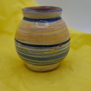 K&ouml;nnte beinhalten: Eine kleine, handbemalte Keramikvase mit rundem K&ouml;rper und einer weiten &Ouml;ffnung. Die Vase ist mit blauen, gelben und wei&szlig;en Streifen verziert.