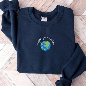 Puede incluir: Una sudadera azul marino con una Tierra bordada en verde y azul y el texto "respeta a tu madre" en la parte delantera.