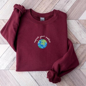 Puede incluir: Una sudadera color burdeos con el texto "respect your mother" bordado en la parte delantera, con un globo terr&aacute;queo bordado en verde y azul.