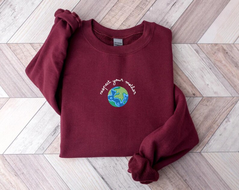 Puede incluir: Una sudadera color burdeos con el texto "respect your mother" bordado en la parte delantera, con un globo terr&aacute;queo bordado en verde y azul.