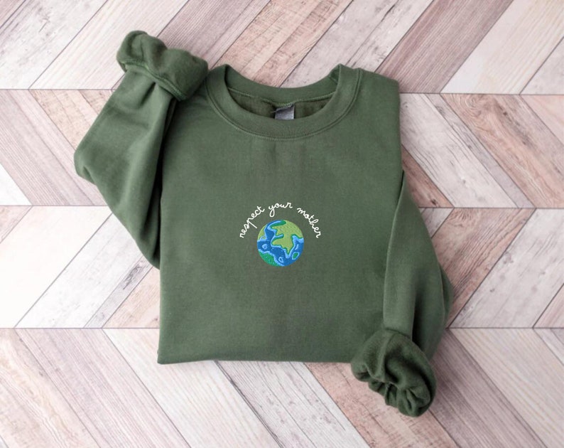 Puede incluir: Una sudadera verde con el texto "respect your mother" bordado en la parte delantera, con una imagen estilizada de la Tierra debajo del texto.