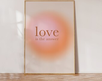 May include: A framed art print with a soft, gradient background in shades of pink and orange. The words "love is the answer" are printed in a warm brown color. The frame is a thin, light brown color.
