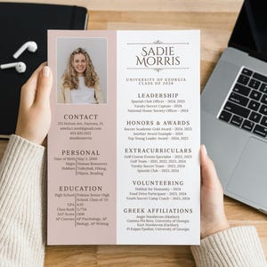 Può includere: Un curriculum vitae tenuto da una persona, con una foto, informazioni di contatto e sezioni per dati personali, istruzione, leadership, onori, attività extrascolastiche, volontariato e affiliazioni greche. Il curriculum è su una superficie di legno con un laptop e un taccuino.