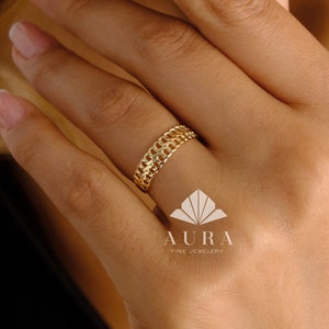 May include: A gold ring with a chain-link design. The ring is worn on a person's finger.