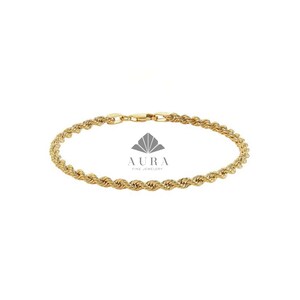May include: A gold rope chain bracelet featuring a twisted, textured link design with a secure lobster claw clasp. The center of the bracelet displays a gray logo with the text AURA FINE JEWELRY positioned above the chain links.