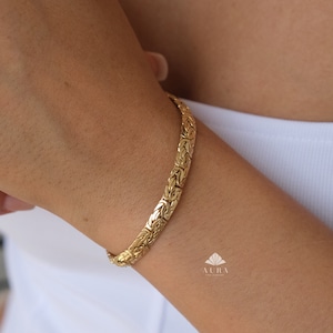 May include: A gold chain bracelet with a woven design. The bracelet is on a person's wrist.