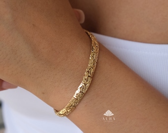 Puede incluir: Un brazalete de cadena de oro con un diseño tejido. El brazalete está en la muñeca de una persona.