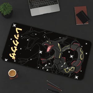 May include: Black rectangular desk mat featuring a stylized illustration of a dragon with red and gold accents, and Japanese text. The design includes a starry background. A laptop, notebook, and coffee cup are also visible.