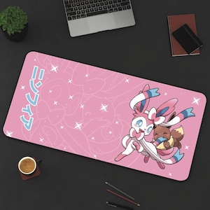 May include: Pink mouse pad with a white outline of a Pokemon character with pink ears and a blue bow. The character is holding a smaller Pokemon character with brown ears and a pink bow. The text "ニンテン" is written in Japanese on the mouse pad.