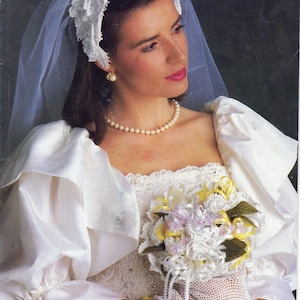 May include: A bride in a white wedding dress with a veil and a floral headpiece. She wears a pearl necklace and earrings. The bouquet is white, yellow, and lavender. The gloves are white crochet.
