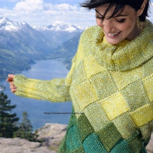 May include: A woman wearing a hand-knitted sweater with a geometric pattern in shades of yellow and green. The sweater has a cowl neck and long sleeves. The background features a mountain range and a lake.