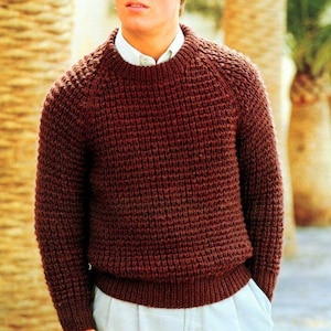 Puede incluir: Un suéter de punto grueso de color burdeos con cuello redondo. El suéter tiene un patrón texturizado y se usa sobre una camisa blanca con cuello. Las palabras "CHUNKY" y "Easy knit" son visibles. Una prenda cálida y cómoda.
