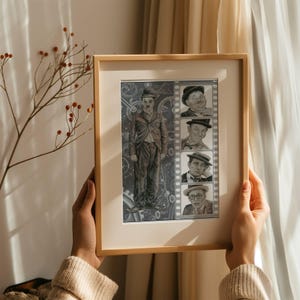 Op de afbeelding: Ingelijste zwart-wit print met Charlie Chaplin en andere vintage filmstills. Het kunstwerk zit in een licht houten frame. De print heeft een vintage esthetiek, met een gedetailleerde illustratie van Chaplin en portretten in filmstripstijl.