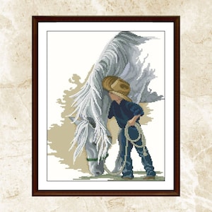 May include: Cross-stitch artwork of a young person in a cowboy hat and dark blue clothing, holding a lasso, next to a white horse. The horse is lowered, and the artwork is framed in a dark brown frame.