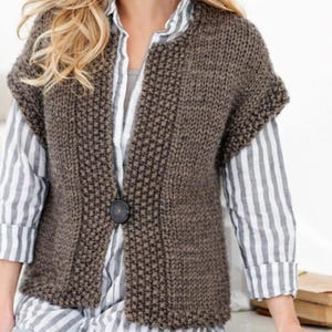 May include: A brown knitted waistcoat with a single large button. The waistcoat features a textured stitch and short sleeves. It is worn over a striped shirt. The style is casual and comfortable, suitable for layering.