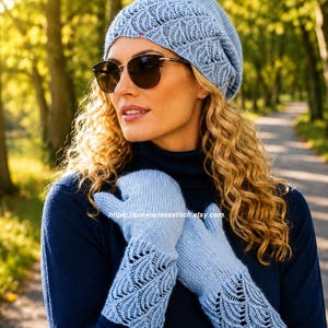 Könnte beinhalten: Eine hellblaue Strickmütze und ein passendes Paar Fäustlinge mit einem zarten, sich wiederholenden fächerartigen Spitzenmuster. Die Accessoires sind aus weichem Garn gefertigt, wobei sich das Spitzendetail auf der Mütze und an den Bündchen befindet.